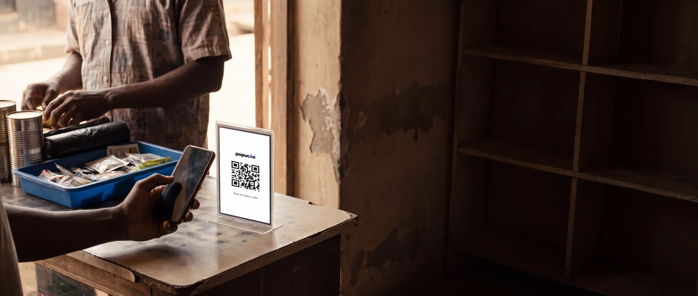 Generated illustration. A carrier's counter card on a Lagos shop counter showing a Popucáo code, with a customer raising their phone to scan it.